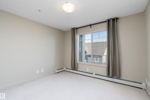 This room features neutral-toned walls, a window with blinds and curtains, and baseboard heating - 309 4008 Savaryn Drive, Edmonton, AB - Indoor Photo Showing Other Room