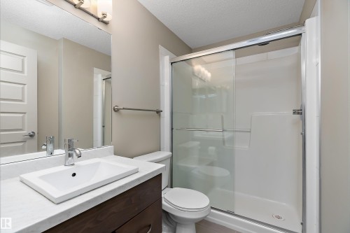 Bathroom featuring a dark wood vanity with a white countertop and rectangular sink, an overhead vanity light, and a glass-enclosed shower - 309 4008 Savaryn Drive, Edmonton, AB - Indoor Photo Showing Bathroom