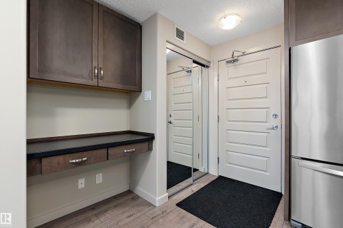 Entryway featuring wood plank flooring, a built-in desk with drawers, overhead cabinetry, and a full-length mirrored closet - 309 4008 Savaryn Drive, Edmonton, AB - Indoor