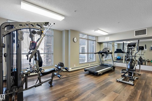 The property features a dedicated fitness area with wood-style flooring, large windows with blinds, and recessed lighting - 309 4008 Savaryn Drive, Edmonton, AB - Indoor Photo Showing Gym Room