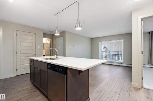 The open concept living area features wood-style flooring and a sliding glass door leading to a balcony - 309 4008 Savaryn Drive, Edmonton, AB - Indoor Photo Showing Kitchen With Double Sink
