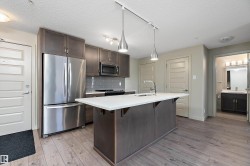 The kitchen features modern stainless steel appliances, dark wood cabinetry, and a large island with a white countertop - 
