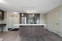 The kitchen features a central island with a white countertop and pendant lighting, stainless steel appliances, and dark cabinetry - 