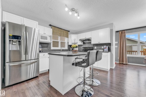 The kitchen features white cabinetry, dark countertops, and stainless steel appliances, including a refrigerator and microwave - 607 Allard Boulevard, Edmonton, AB - Indoor Photo Showing Kitchen