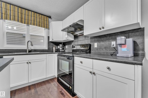 The kitchen features white cabinetry, dark countertops, a dark tile backsplash, and a window above the sink - 607 Allard Boulevard, Edmonton, AB - Indoor Photo Showing Kitchen With Double Sink