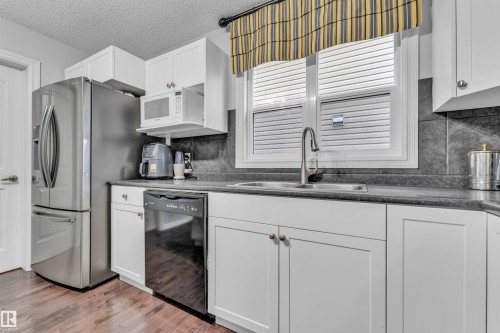 The kitchen features a stainless steel refrigerator, white cabinetry, a dishwasher, and a sink with a window above - 607 Allard Boulevard, Edmonton, AB - Indoor Photo Showing Kitchen With Double Sink