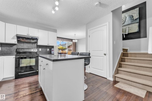 Kitchen with white cabinetry, dark countertops, dark backsplash, and hardwood floors - 607 Allard Boulevard, Edmonton, AB - Indoor Photo Showing Kitchen