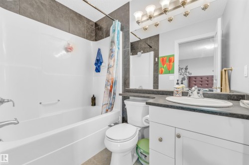 Bathroom featuring a white bathtub, a tiled shower surround, a white toilet, and a vanity with a dark countertop and a white sink - 607 Allard Boulevard, Edmonton, AB - Indoor Photo Showing Bathroom