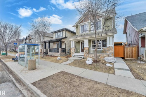 The property features a two-story exterior with light green siding and stone accents, a covered front porch with white railings, and a landscaped front yard with decorative rocks - 607 Allard Boulevard, Edmonton, AB - Outdoor With Deck Patio Veranda With Facade