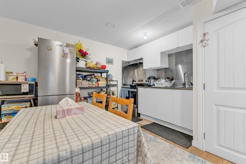 The kitchen features white cabinetry, a stainless steel refrigerator, and a sink with a wall-mounted faucet - 607 Allard Boulevard, Edmonton, AB - Indoor Photo Showing Kitchen