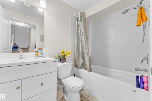 This bathroom features a white vanity with a rectangular sink, a toilet, and a bathtub with white tiled walls - 607 Allard Boulevard, Edmonton, AB - Indoor Photo Showing Bathroom