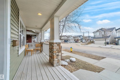 The property features a charming front porch with light-colored siding, a white railing, and a stone-clad column - 607 Allard Boulevard, Edmonton, AB - Outdoor With Deck Patio Veranda