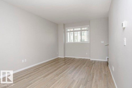 This interior space features light-toned walls, wood-look flooring, and a window with blinds providing natural light - 99 320 Secord Boulevard, Edmonton, AB - Indoor Photo Showing Other Room
