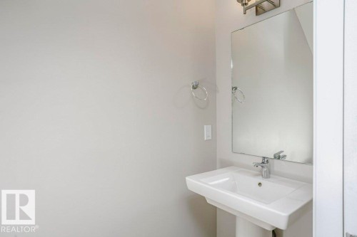 Bathroom featuring a pedestal sink with a chrome faucet, a rectangular mirror, and a wall-mounted light fixture - 99 320 Secord Boulevard, Edmonton, AB - Indoor Photo Showing Bathroom