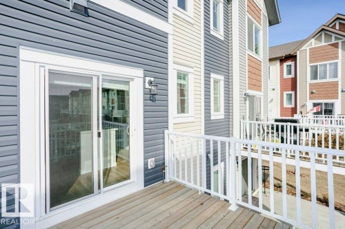 The property features a private deck with white railings, a sliding glass door for access, and exterior siding in a combination of blue and white tones - 99 320 Secord Boulevard, Edmonton, AB - Outdoor With Deck Patio Veranda
