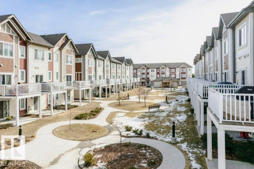 The property features a series of townhome-style residences with private balconies, set around a landscaped courtyard with pathways and a central gazebo structure - 99 320 Secord Boulevard, Edmonton, AB - Outdoor