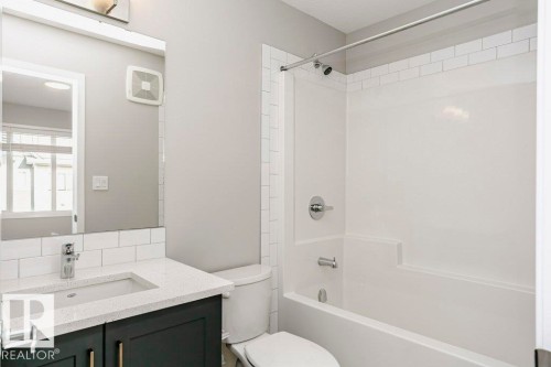 The bathroom features a modern vanity with a light-colored countertop and dark cabinetry, a white subway tile backsplash, and a bathtub with an integrated shower - 99 320 Secord Boulevard, Edmonton, AB - Indoor Photo Showing Bathroom