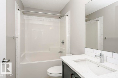 Bathroom featuring a white subway tile backsplash, a vanity with a white countertop and an integrated sink, and a white bathtub with a shower - 99 320 Secord Boulevard, Edmonton, AB - Indoor Photo Showing Bathroom