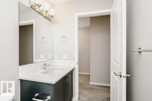 The bathroom features a vanity with a white countertop and a rectangular sink, complemented by a large mirror and modern light fixture - 99 320 Secord Boulevard, Edmonton, AB - Indoor Photo Showing Bathroom