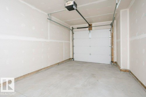 The property includes a garage with a concrete floor, an automatic garage door opener, and unfinished drywall walls - 99 320 Secord Boulevard, Edmonton, AB - Indoor Photo Showing Garage