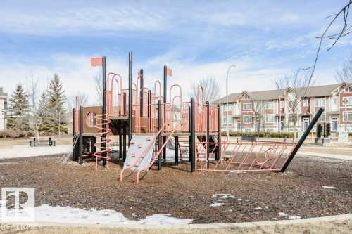 This community features a playground with a ship-themed structure, set on a dark ground covering, and surrounded by bare trees - 99 320 Secord Boulevard, Edmonton, AB - Outdoor