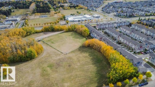 Aerial view showcasing the property's location within a developed neighborhood, featuring surrounding green spaces with trees, and a residential street with parked cars - 99 320 Secord Boulevard, Edmonton, AB - Outdoor With View
