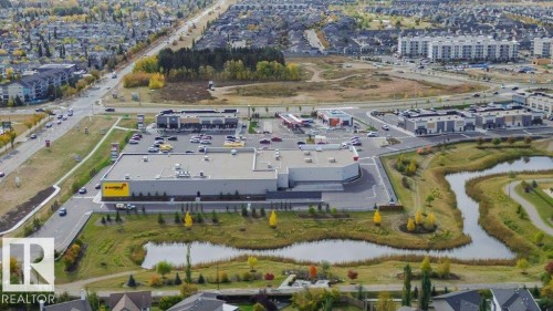 Aerial view showcasing the property's surrounding commercial buildings, a paved road with vehicles, and green spaces featuring ponds - 99 320 Secord Boulevard, Edmonton, AB - Outdoor With View