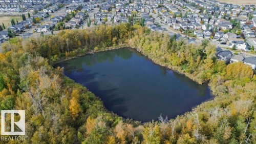 Aerial view showcasing the surrounding neighborhood, featuring a body of water encircled by trees, and residential properties with varied roof colors - 99 320 Secord Boulevard, Edmonton, AB - Outdoor With Body Of Water With View