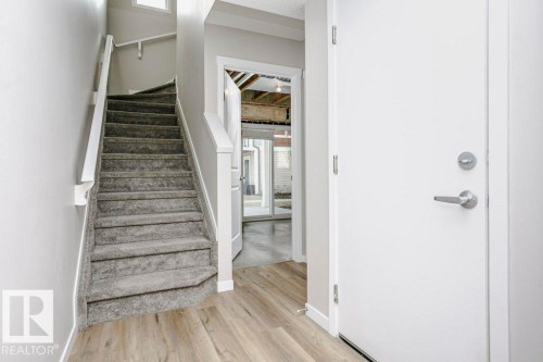 The entryway features light wood-style flooring, a carpeted staircase with white railings, and a white door with a silver handle - 99 320 Secord Boulevard, Edmonton, AB - Indoor Photo Showing Other Room