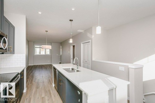 The kitchen features a large island with a sink, stainless steel appliances, and sleek cabinetry - 99 320 Secord Boulevard, Edmonton, AB - Indoor Photo Showing Kitchen With Double Sink With Upgraded Kitchen