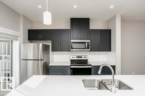 The kitchen features stainless steel appliances, dark cabinetry, and white countertops - 99 320 Secord Boulevard, Edmonton, AB - Indoor Photo Showing Kitchen With Stainless Steel Kitchen With Upgraded Kitchen