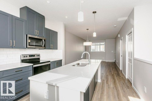 Contemporary kitchen featuring grey cabinetry, white countertops, a subway tile backsplash, and stainless steel appliances - 99 320 Secord Boulevard, Edmonton, AB - Indoor Photo Showing Kitchen With Stainless Steel Kitchen With Double Sink With Upgraded Kitchen