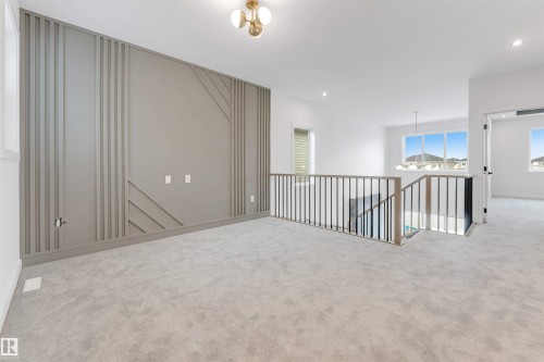 Spacious open area featuring light gray carpeting, a decorative accent wall with paneling, and a contemporary light fixture - 20 Meadowgrove Landing, Spruce Grove, AB - Indoor Photo Showing Other Room