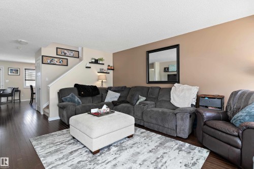 Living area featuring dark wood flooring, a light-colored area rug, and a staircase with a white railing - 6822 Cardinal Link, Edmonton, AB - Indoor Photo Showing Living Room