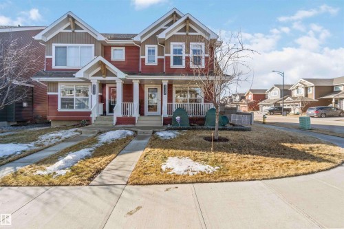 The property features a red and brown exterior with white trim, a covered front porch with white railings, and a paved walkway leading to the entrance - 4750 Crabapple Run, Edmonton, AB - Outdoor With Facade