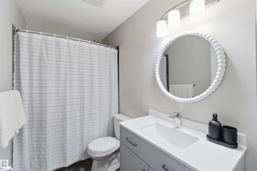 The bathroom features a modern vanity with a white countertop and a circular mirror with a decorative frame - 4750 Crabapple Run, Edmonton, AB - Indoor Photo Showing Bathroom
