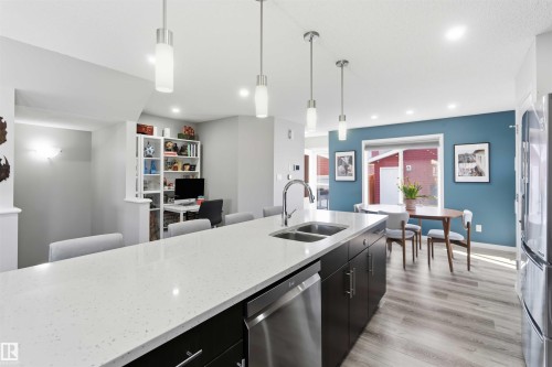 Kitchen featuring a large island with a light-colored countertop and double sink, dark cabinetry, and stainless steel appliances - 4750 Crabapple Run, Edmonton, AB - Indoor Photo Showing Kitchen With Stainless Steel Kitchen With Double Sink With Upgraded Kitchen