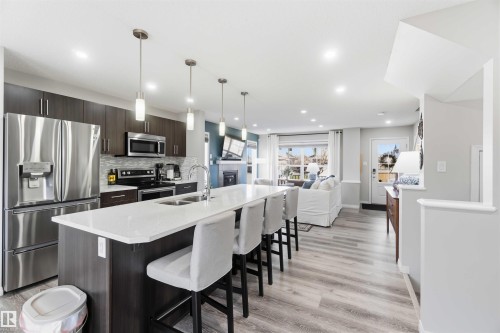 The open-concept main living area features a kitchen with a large island with seating, stainless steel appliances, and dark wood cabinetry - 4750 Crabapple Run, Edmonton, AB - Indoor Photo Showing Kitchen With Stainless Steel Kitchen With Double Sink With Upgraded Kitchen