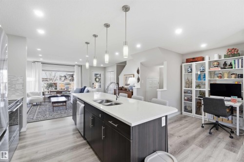 Open concept living space featuring a kitchen with a large island and stainless steel appliances, a living room with a large window, and light wood-style flooring throughout - 4750 Crabapple Run, Edmonton, AB - Indoor Photo Showing Kitchen With Double Sink With Upgraded Kitchen