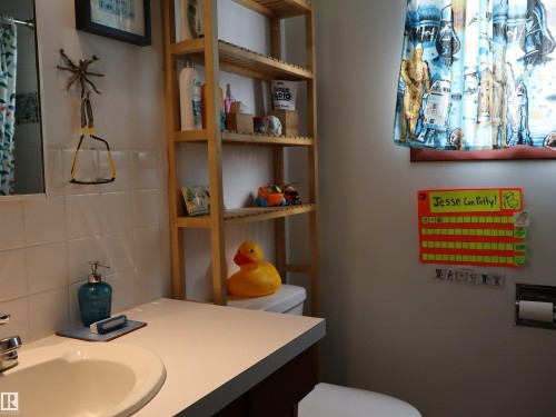 Bathroom featuring a white vanity with an integrated sink, a wall-mounted mirror, and white tiled walls - 4315 56 Avenue, Barrhead, AB - Indoor Photo Showing Bathroom