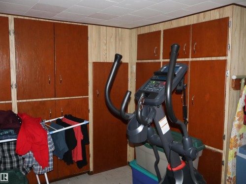 This room features wood paneling and extensive built-in cabinetry with brown doors and silver hardware, offering abundant storage - 4315 56 Avenue, Barrhead, AB - Indoor