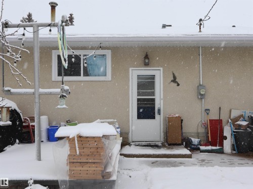 The property features an exterior with a stucco finish, a white storm door, and a white-framed window - 4315 56 Avenue, Barrhead, AB - Outdoor