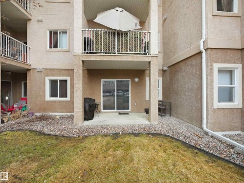 The property features a ground-level patio with sliding glass doors, a grass area, and a rock border - 106 2305 35A Avenue Nw, Edmonton, AB - Outdoor With Exterior