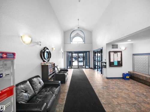 Spacious common area featuring tiled flooring, a high vaulted ceiling, and ample natural light from the entrance - 106 2305 35A Avenue Nw, Edmonton, AB - Indoor Photo Showing Other Room