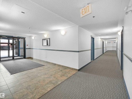 The property features a well-maintained entrance area with glass doors, leading to a hallway with tiled flooring and carpeting - 106 2305 35A Avenue Nw, Edmonton, AB - Indoor Photo Showing Other Room