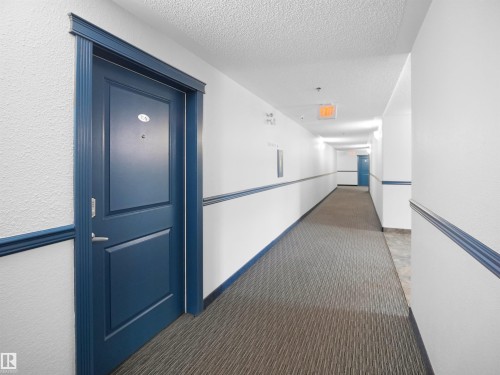 The property features a blue entry door with a door number and a peephole, set within a white textured wall with blue trim - 106 2305 35A Avenue Nw, Edmonton, AB - Indoor Photo Showing Other Room