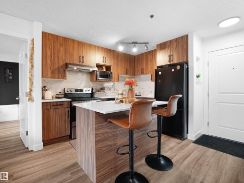 The kitchen features rich wood cabinetry, a white countertop island, and stainless steel appliances - 106 2305 35A Avenue Nw, Edmonton, AB - Indoor Photo Showing Kitchen