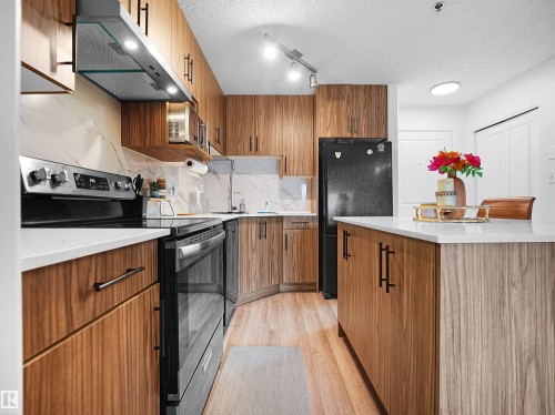 The kitchen features wood cabinetry, a white countertop, a white marble style backsplash, and modern black appliances - 106 2305 35A Avenue Nw, Edmonton, AB - Indoor Photo Showing Kitchen