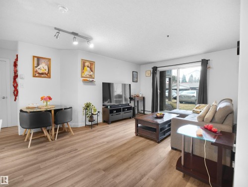 The property features light wood tone flooring throughout, a dining area with a table and chairs, and a living area with a sliding glass door - 106 2305 35A Avenue Nw, Edmonton, AB - Indoor Photo Showing Living Room