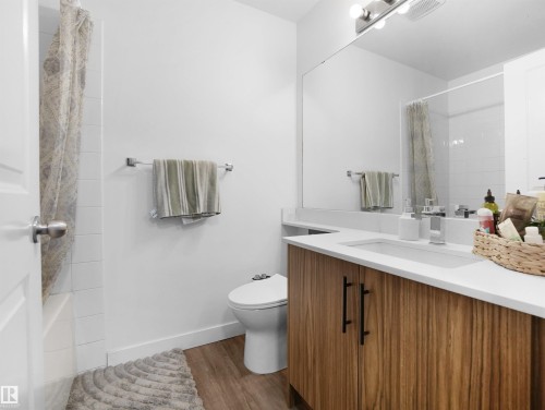 Well-appointed bathroom featuring a modern vanity with a white countertop and natural wood cabinetry, a large mirror, and clean white walls - 106 2305 35A Avenue Nw, Edmonton, AB - Indoor Photo Showing Bathroom